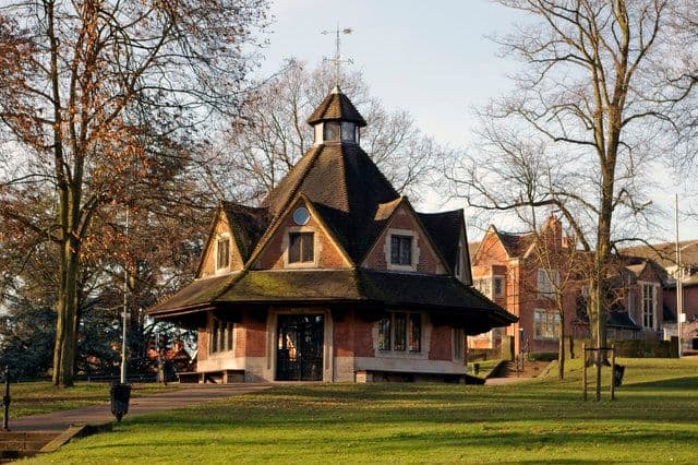 Octagonal brick building with a steep tiled roof and small lantern on a village green.