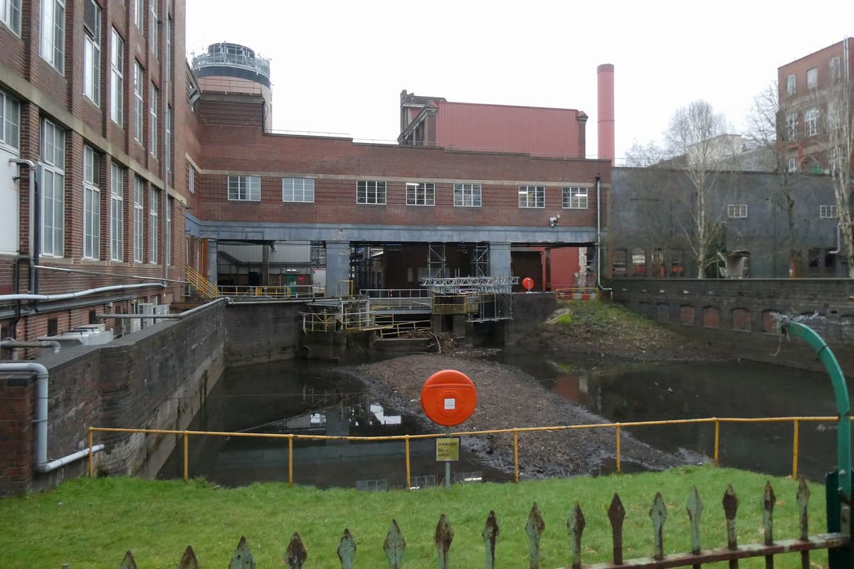 Large brick factory buildings beside a small stream lined with trees.