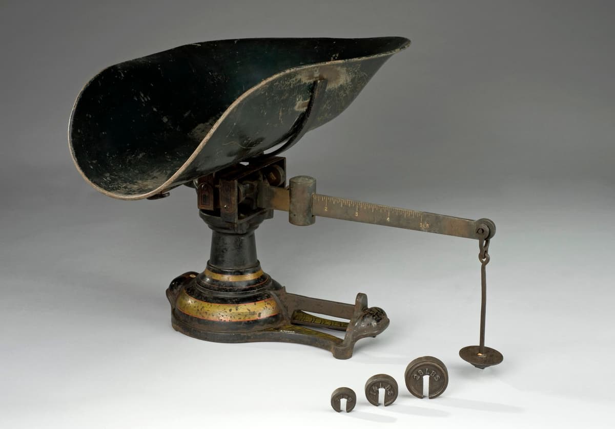 Iron balance scale with a shallow pan for a baby and a set of weights.