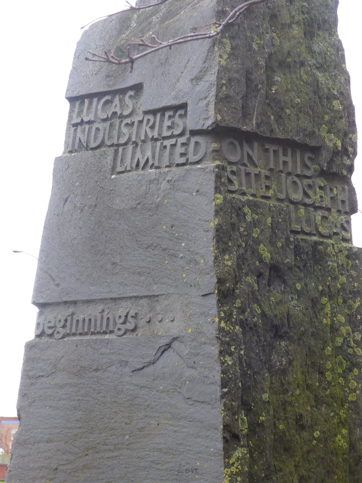 A tall, weathered slate block carved with the words Lucas Industries Limited, On this site Joseph Lucas, and From small beginnings.