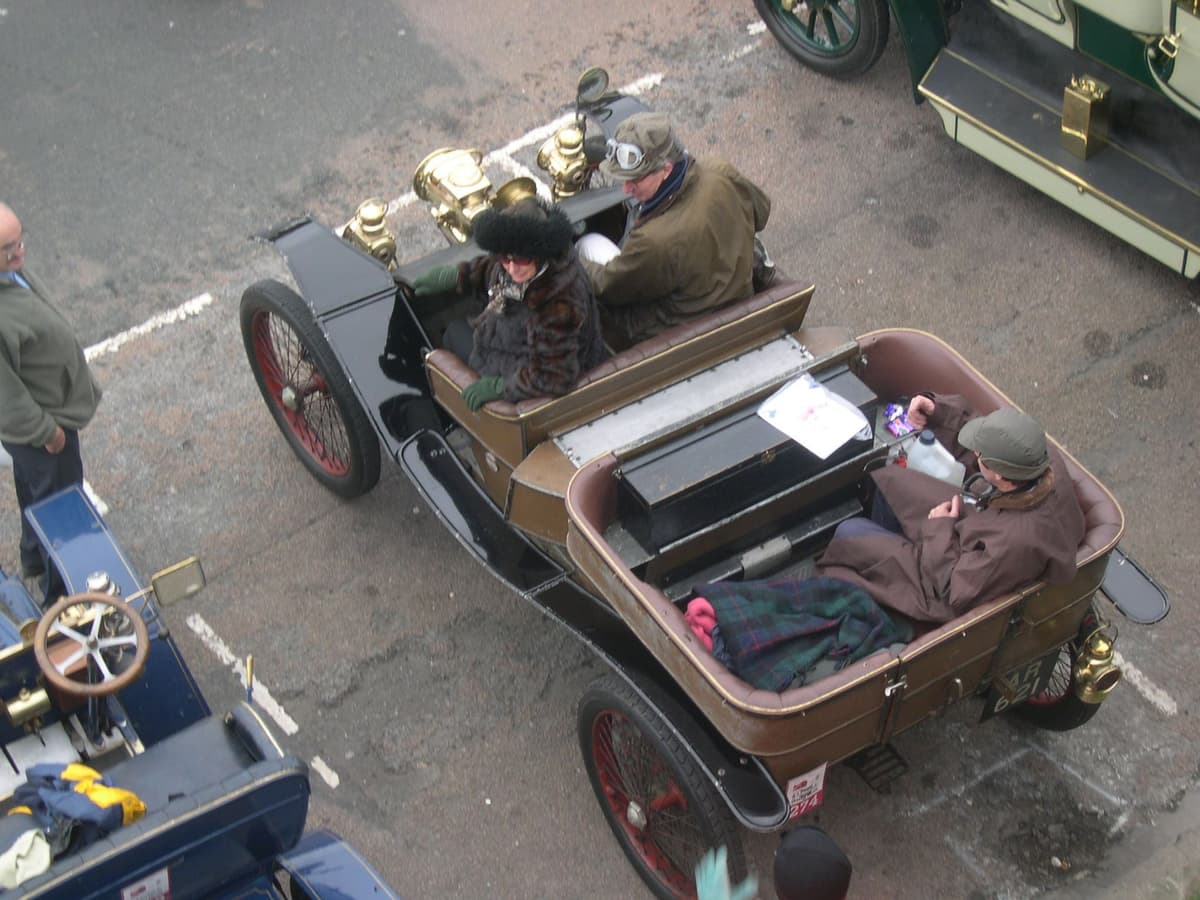 An open veteran car with brass lamps and a rear passenger compartment, seen from above, with its crew aboard.