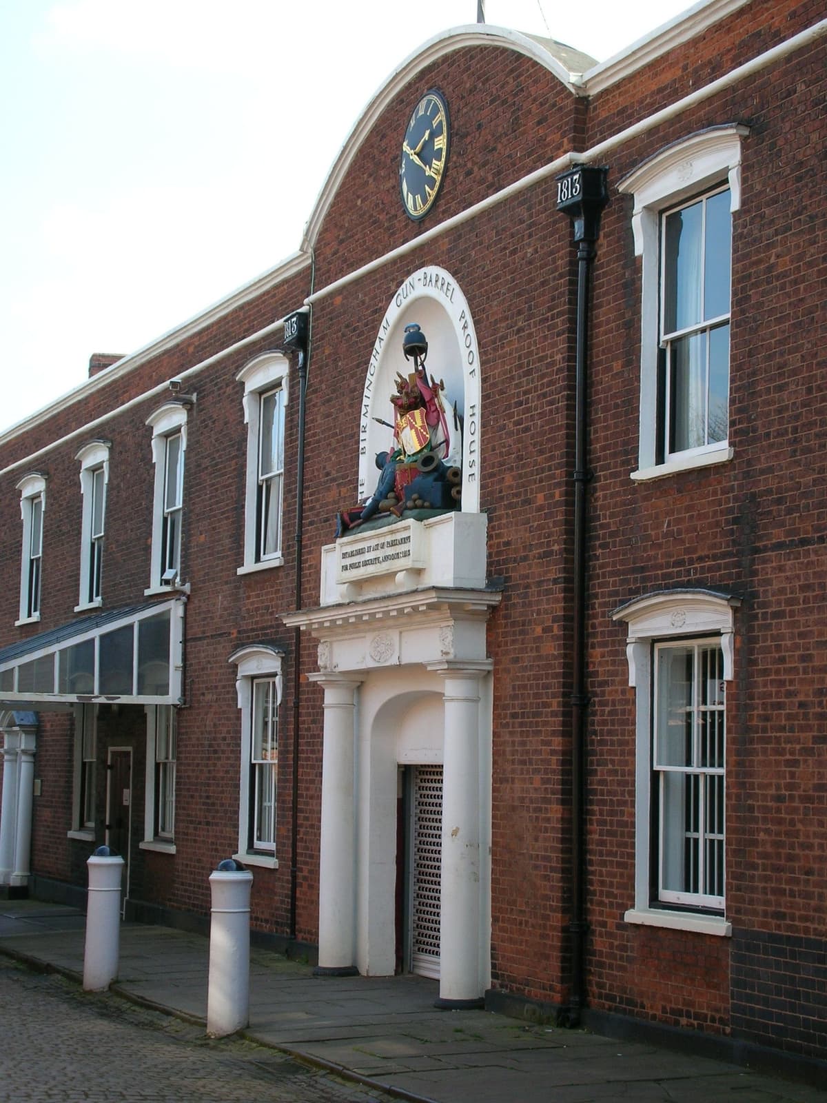 The front of a Georgian brick building with a carved trophy of arms and a clock above the doorway.