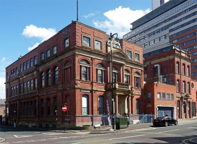 A red-brick Italianate office building with a columned porch and the royal coat of arms above.