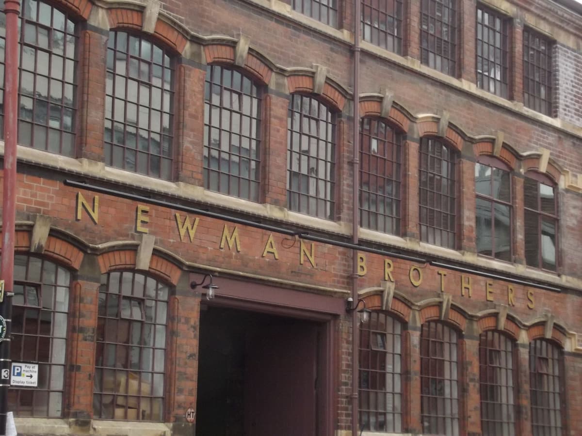 A three-storey red-brick factory front with rows of closely set windows and large wooden cart doors.