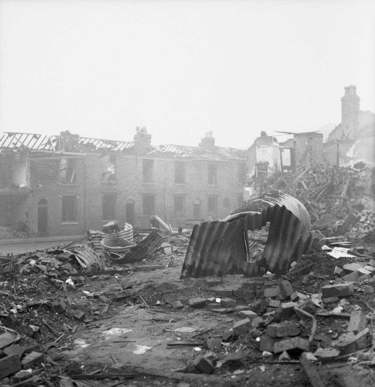 Wartime photograph of rubble and twisted steel shelters among bombed houses.