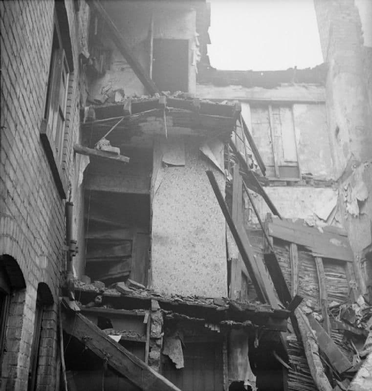Wartime photograph of a terraced house with its side wall blown away, showing the staircase and wallpaper.