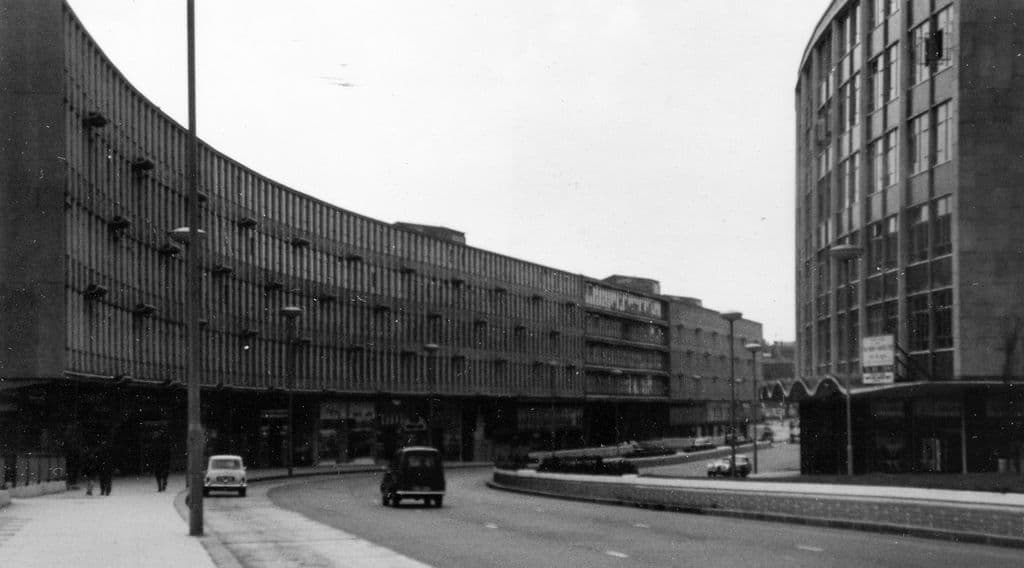 1960s photograph of a new dual carriageway curving past a long modern block of shops and offices.