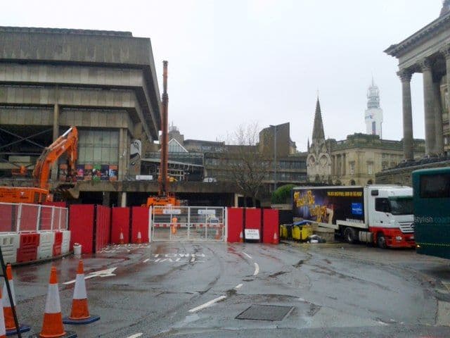 Closed urban road junction with barriers and concrete buildings.