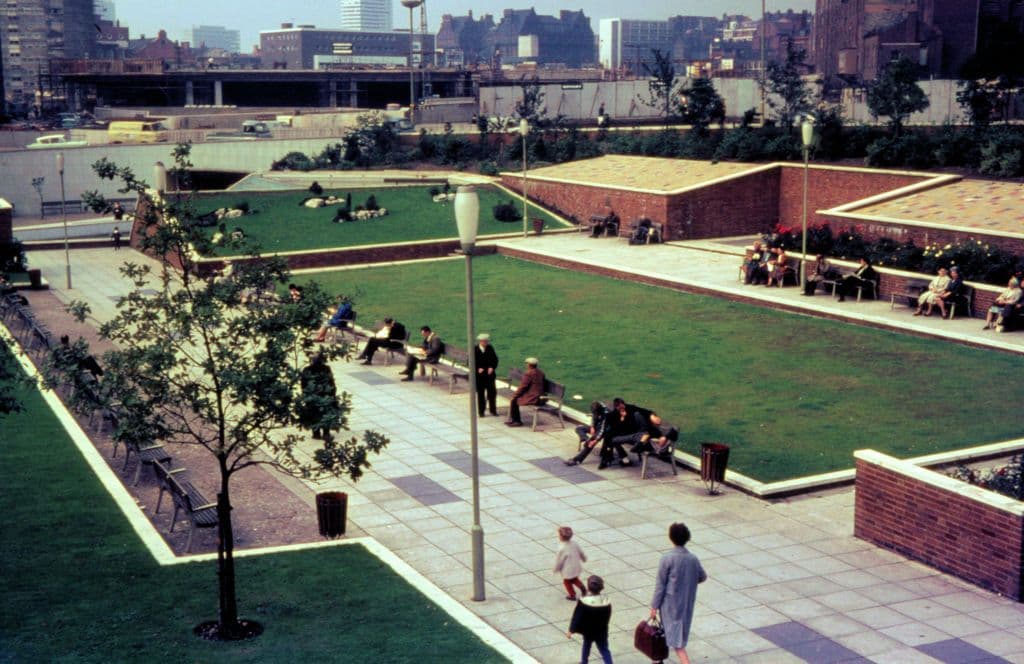 1960s view from a footbridge over a small public garden beside a ring road.