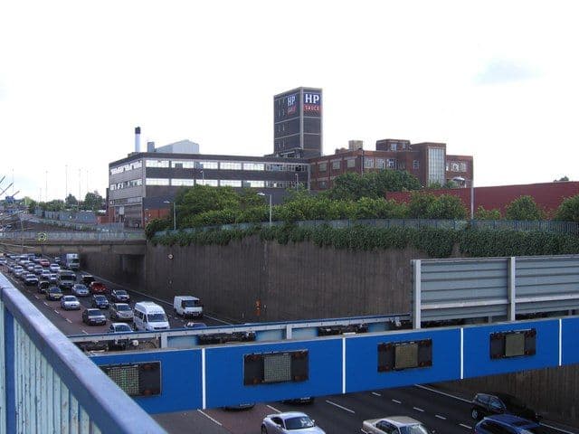 Brick factory with a large HP sign on its roof, with demolition machinery in front.