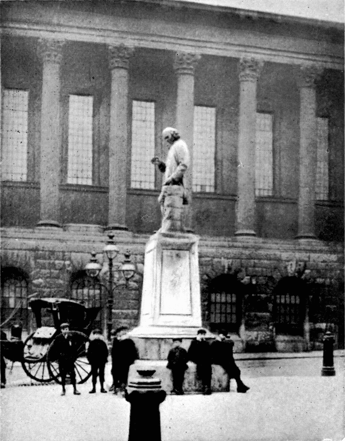 An old printed photograph of a statue of a man in a long coat on a tall pedestal.