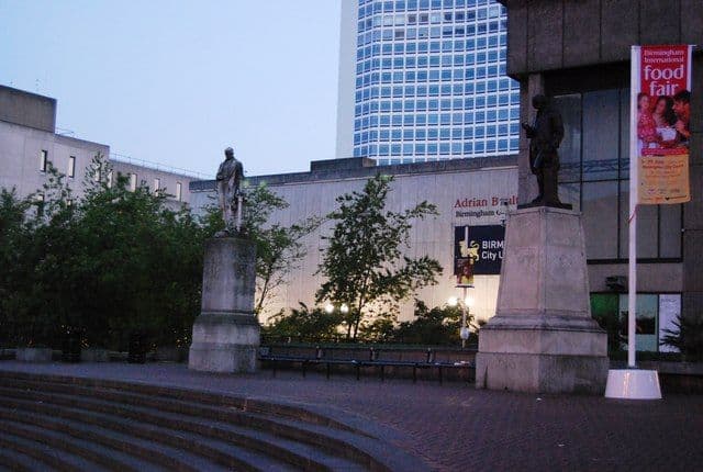 Two statues on plinths in a paved square.