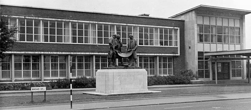 A 1960s view of a civic building with a gilded statue group in front of it.