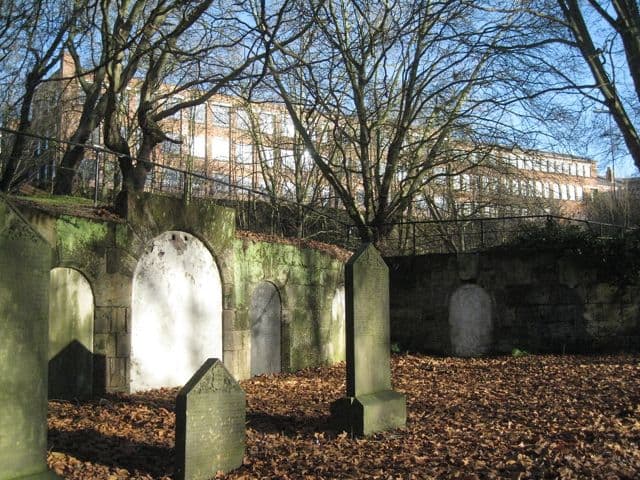 A curving wall of blocked catacomb entrances set into a hillside in a cemetery.