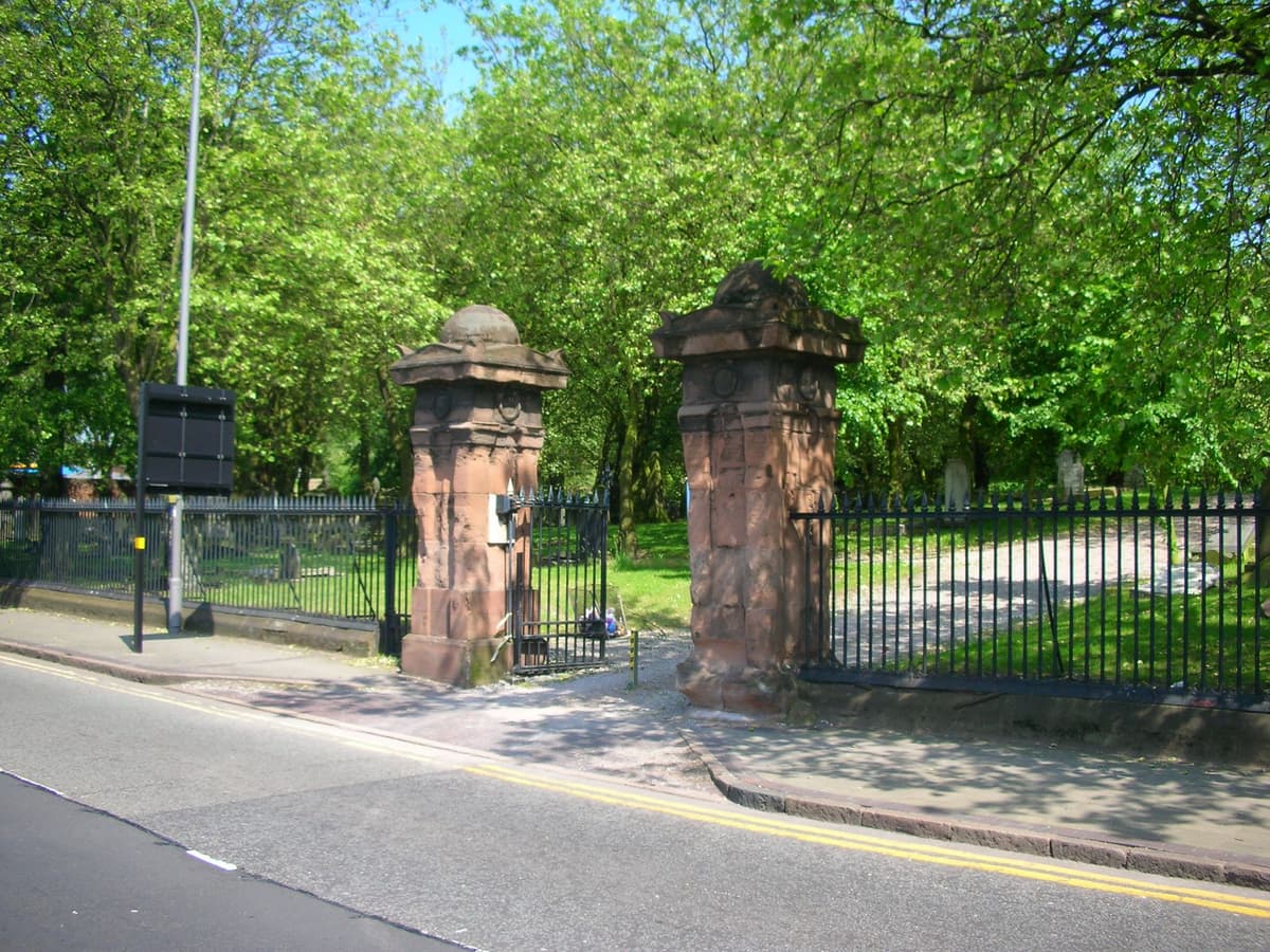 Iron gates and railings between stone piers at a cemetery entrance.