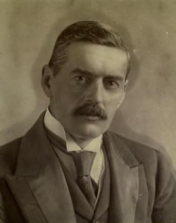 Sepia photograph of a man with dark hair and a moustache, in a three-piece suit and stiff collar.
