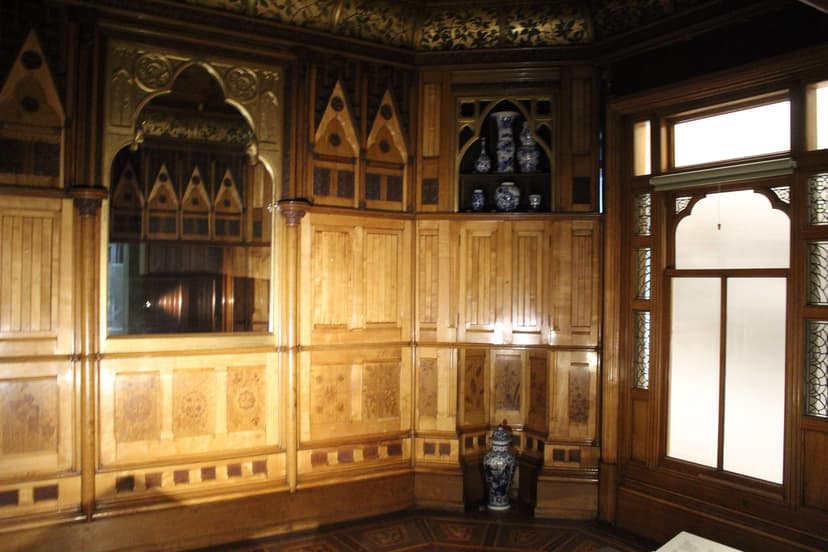 A small room lined with inlaid wooden panelling, a gilded mirror and a marble fireplace.