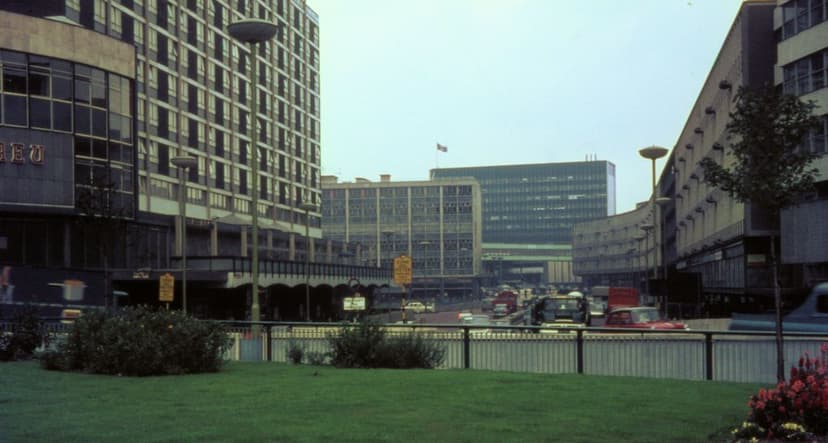View from a grassy roundabout along a dual carriageway lined with new office blocks and a tall hotel, with traffic in the distance.