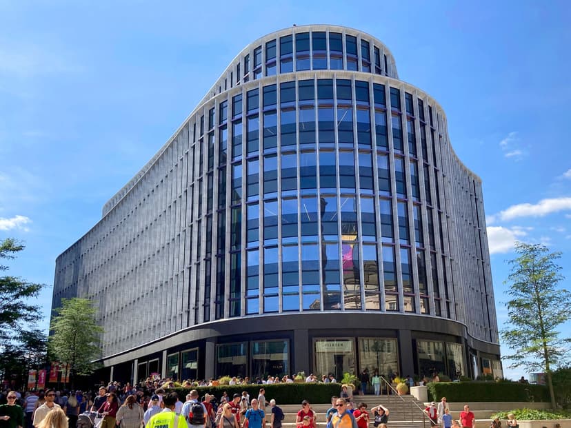 A modern stone-and-glass office building beside a paved square.