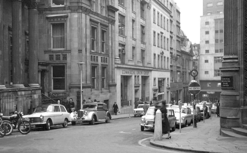 Black-and-white photograph looking down a street of Victorian office buildings with parked cars, towards New Street.