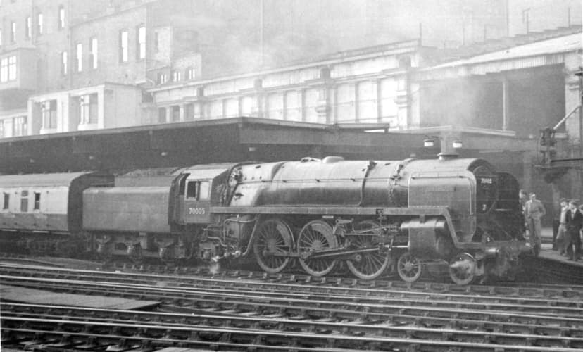 Black-and-white photograph of a steam express locomotive at a platform of a large Victorian station.