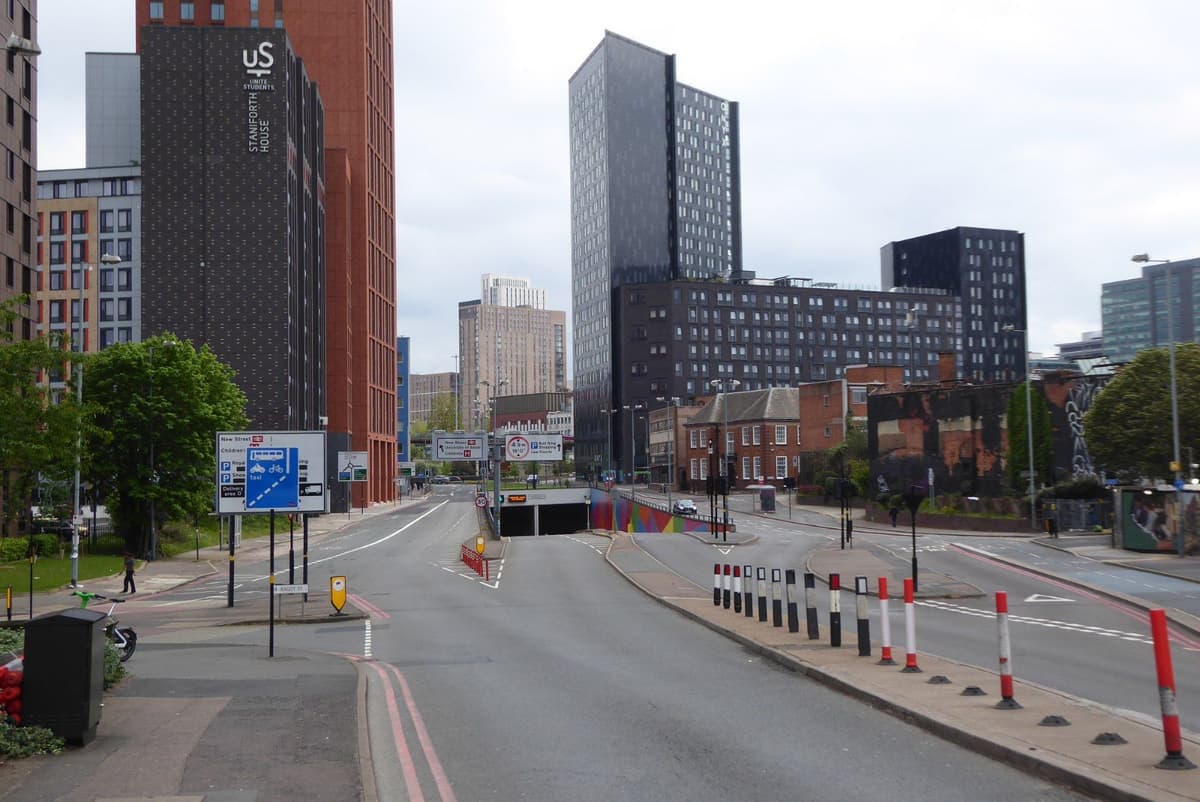A wide city road dipping towards an underpass, with tall modern blocks beyond.