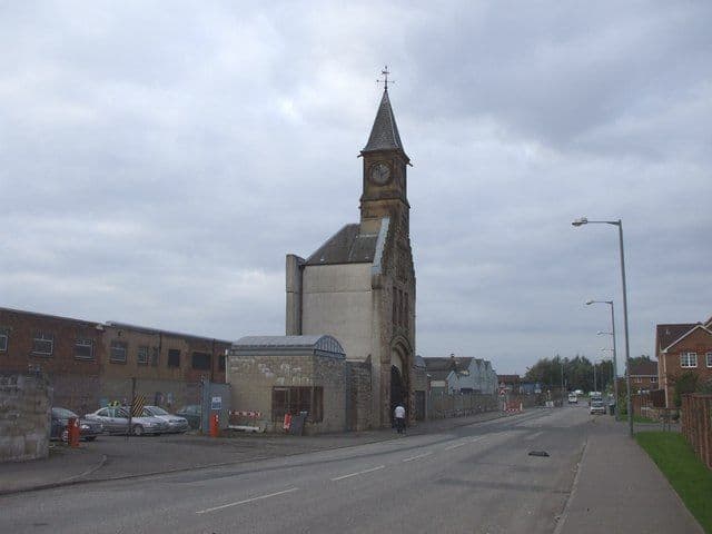 A stone clocktower standing alone beside a road, with an arched opening at its base.