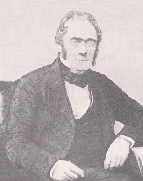 Black-and-white portrait of a seated middle-aged man in a dark Victorian coat.