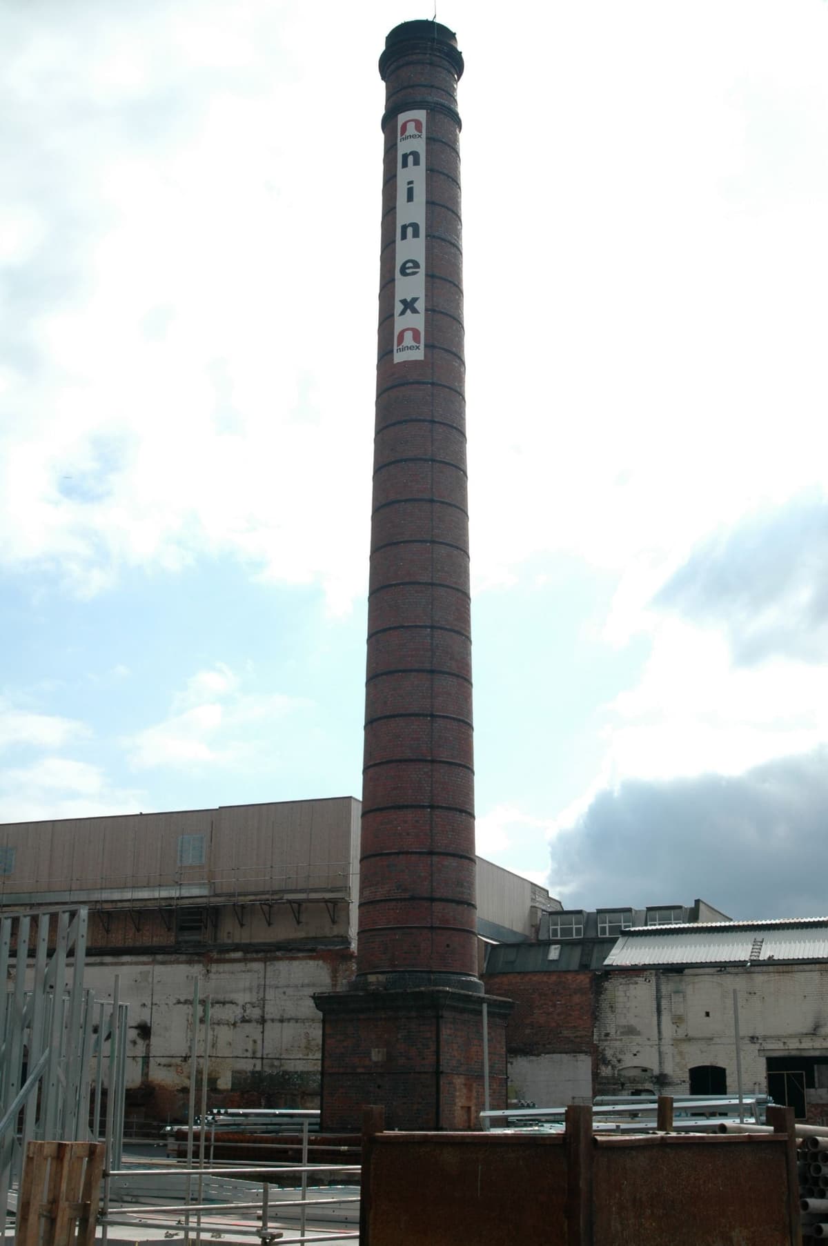Tall square-section brick chimney rising above industrial buildings.