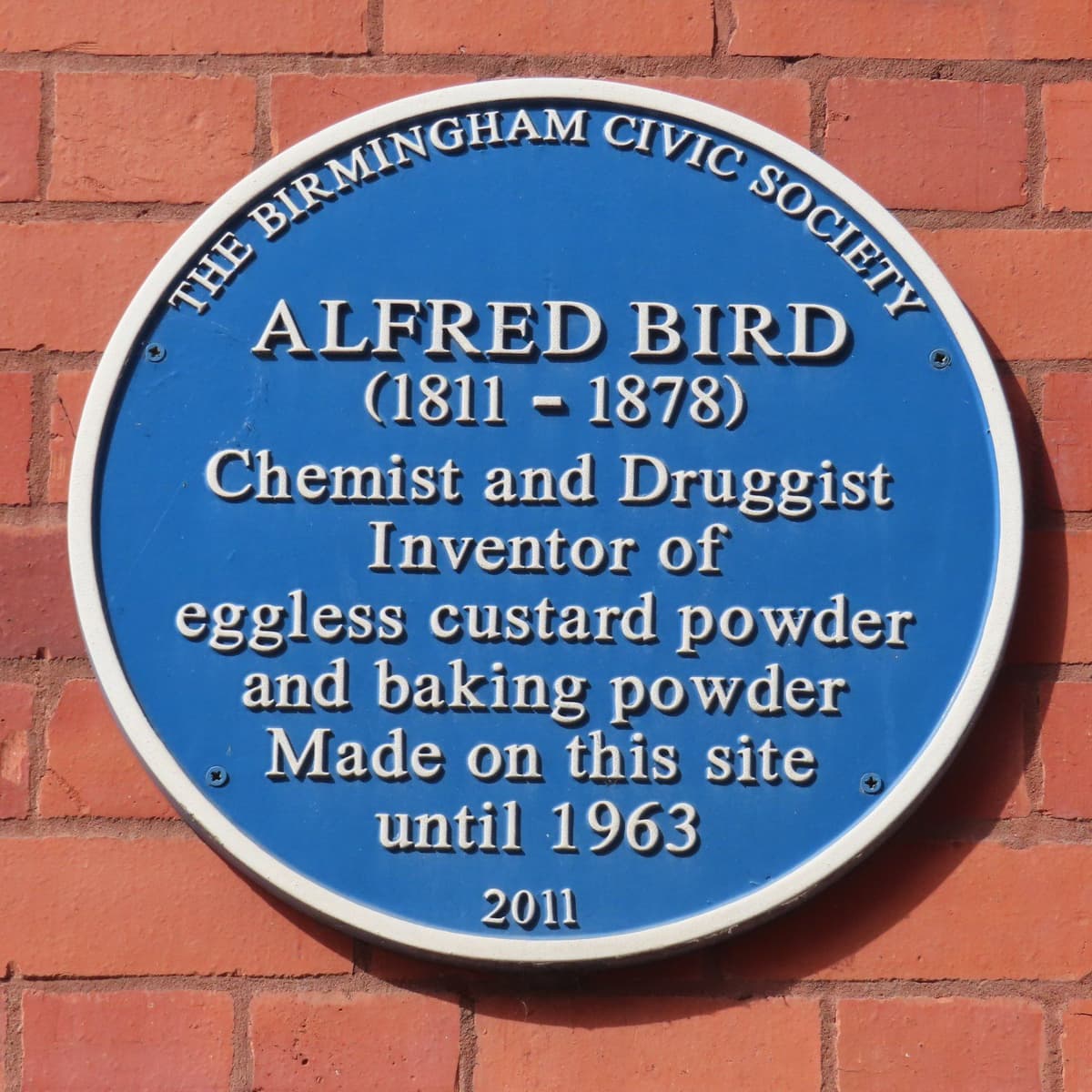 A round blue plaque on a brick wall.