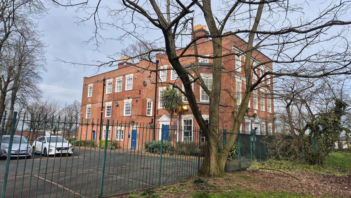 A plain red-brick Georgian house seen through bare trees and railings.