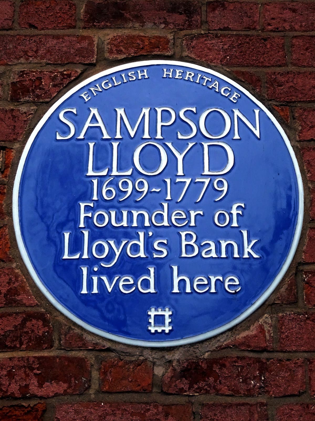 A round blue English Heritage plaque on a brick wall.