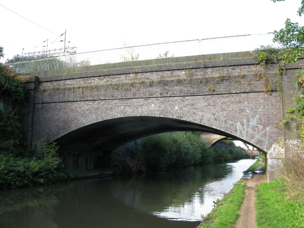 Small brick bridge over a canal inside an industrial site, with brick warehouses either side.