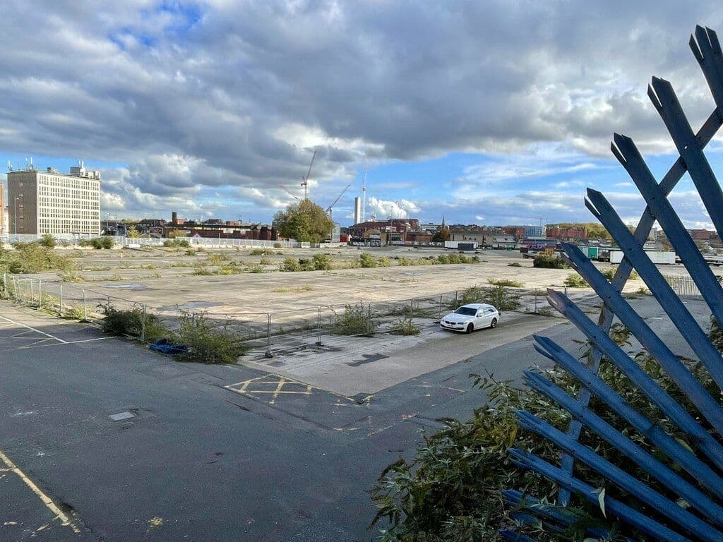 A large cleared building site in a city centre, behind hoardings.