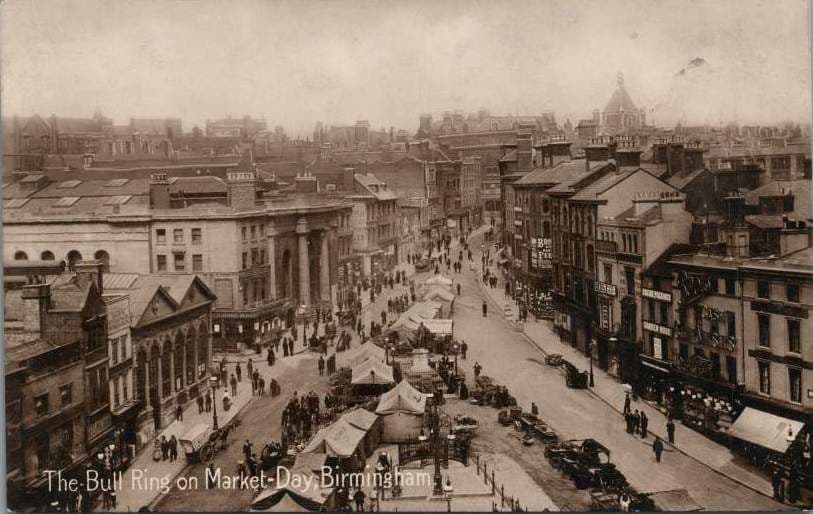 Colour postcard of a crowded street market with Nelson’s statue in the middle, a gabled market building in the foreground and a large classical market hall behind.