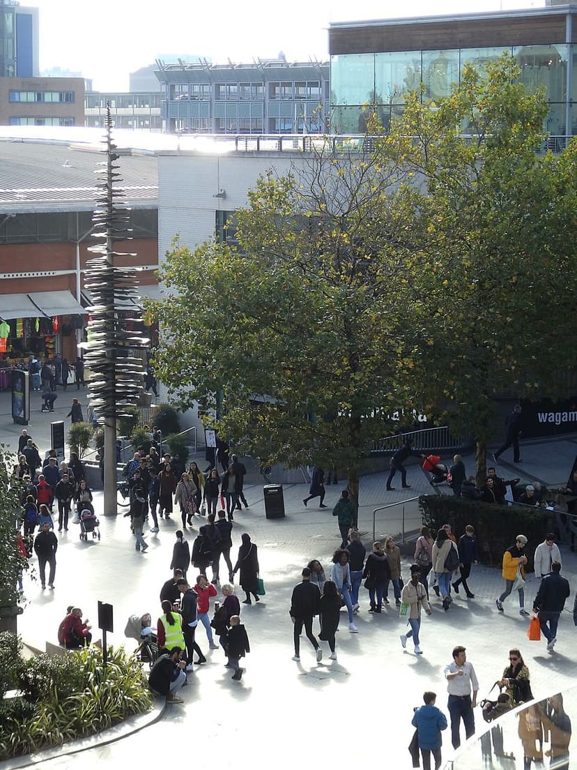 A pedestrian street in a modern shopping centre, with shoppers and glass shopfronts.
