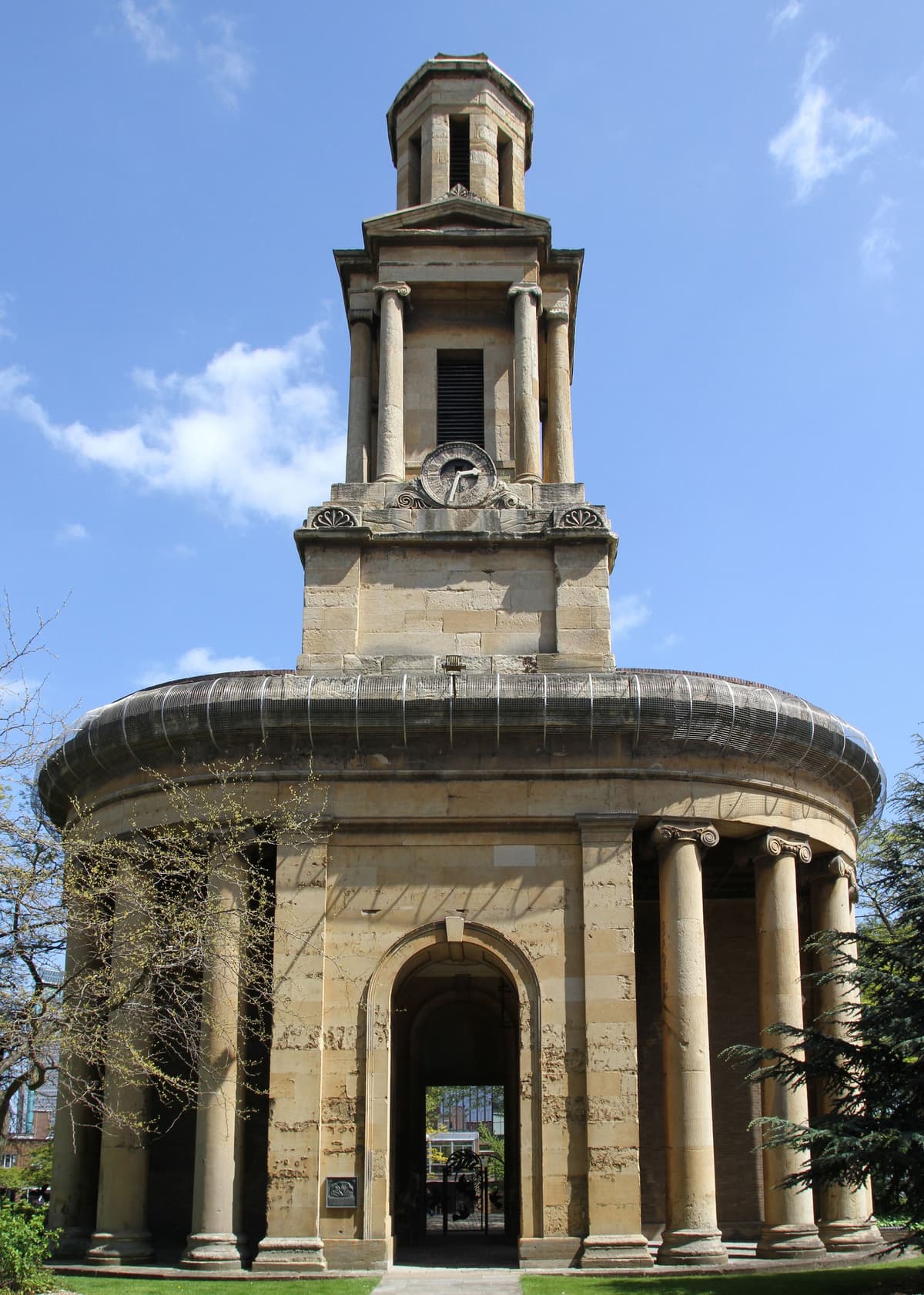 A classical stone tower above a curved colonnade, standing alone among trees.