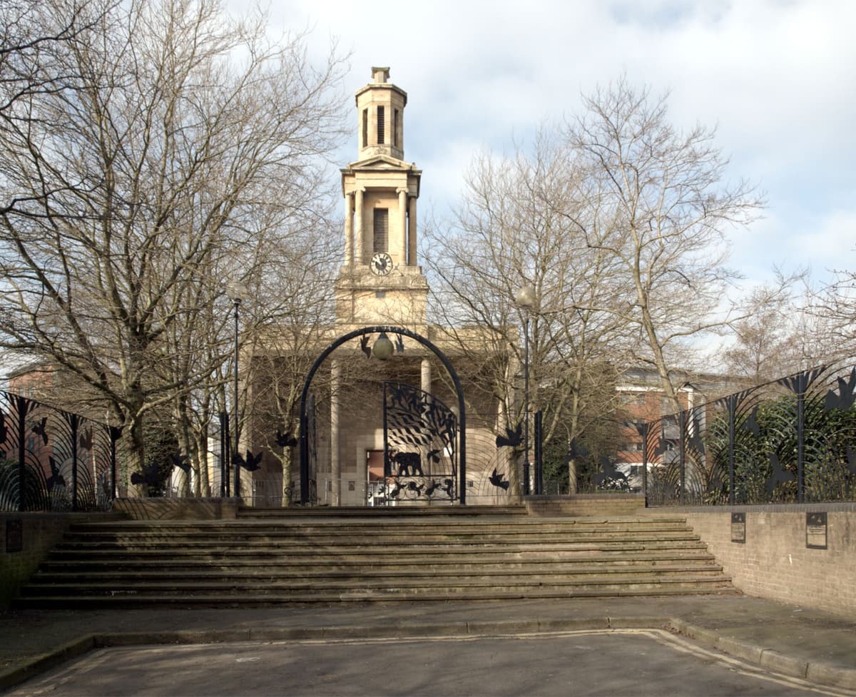 Steps and decorative iron gates leading up through a garden to the back of a stone church tower.