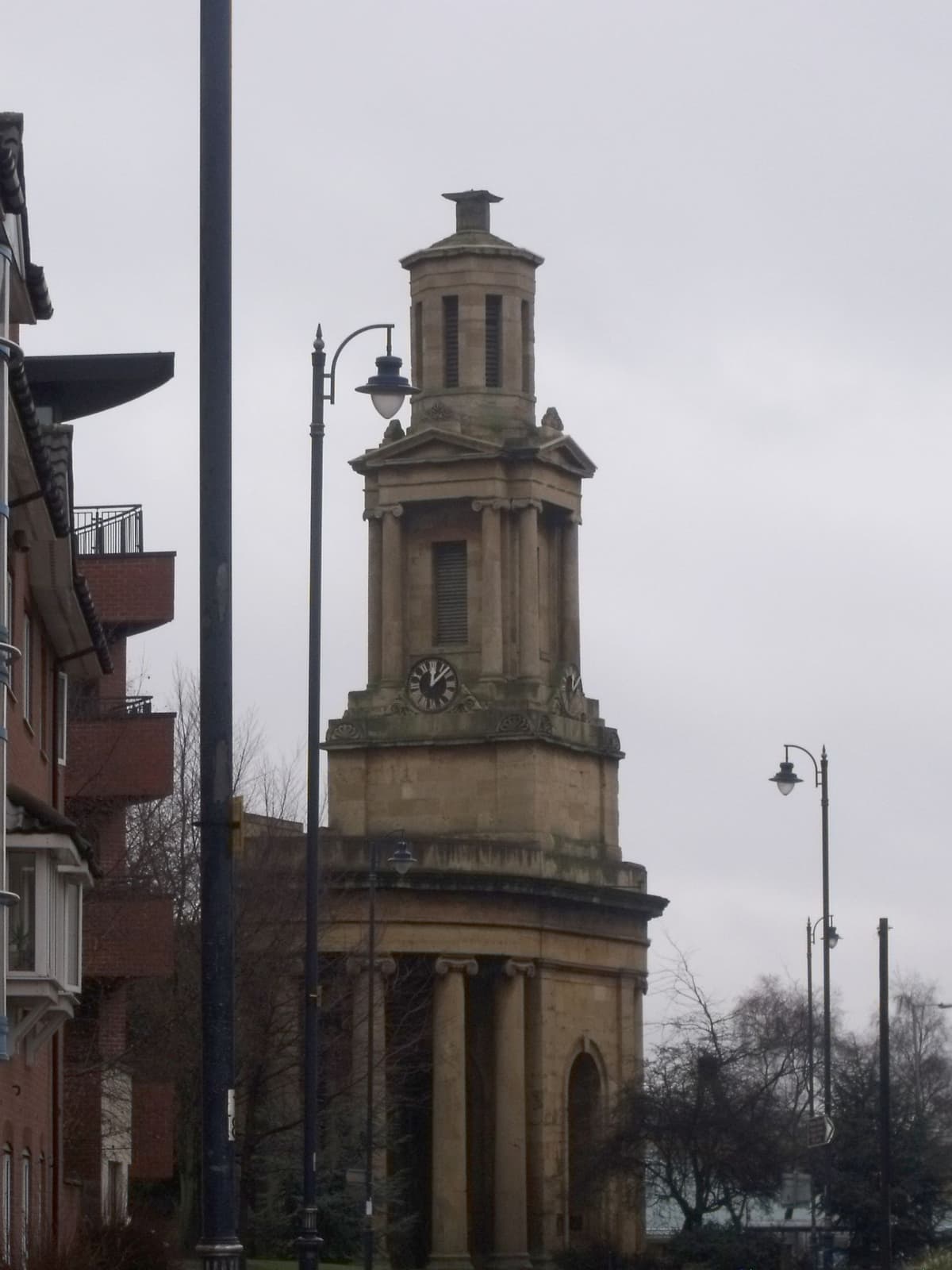 Close view of a classical stone church tower with a clock, above curved Ionic columns.
