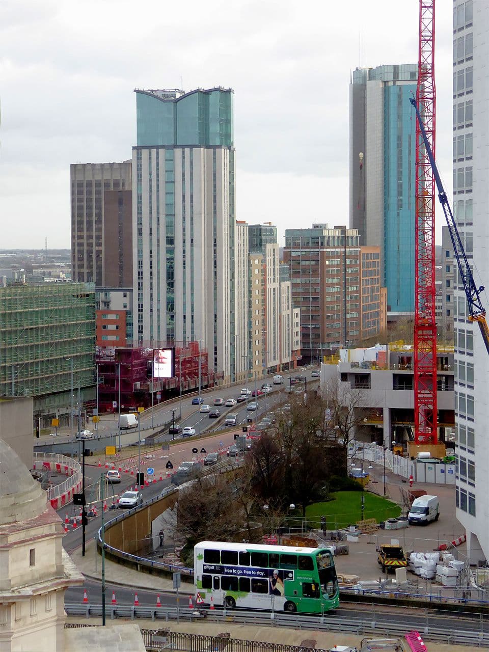 A dual carriageway seen from above, with new tower blocks under construction beside it.