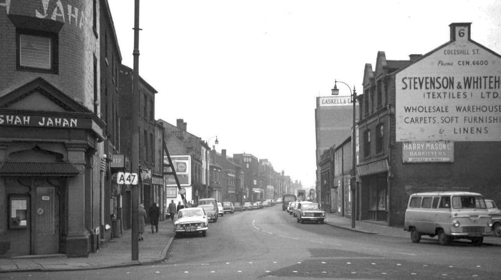Black-and-white photograph of a street of old brick buildings running away from a junction.