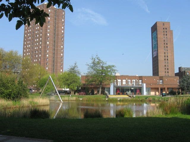 An ornamental lake with grass banks among university buildings.