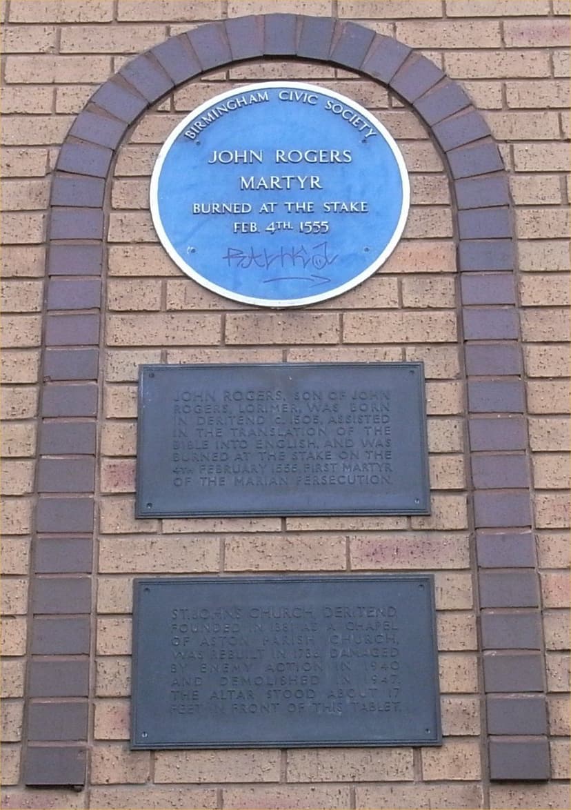 A blue plaque to John Rogers above two bronze tablets set in a brick arch.