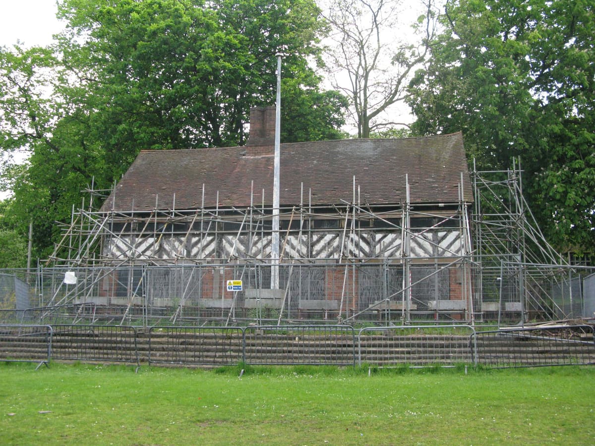 A black-and-white timber-framed building with three gables and a brick ground floor in a park.