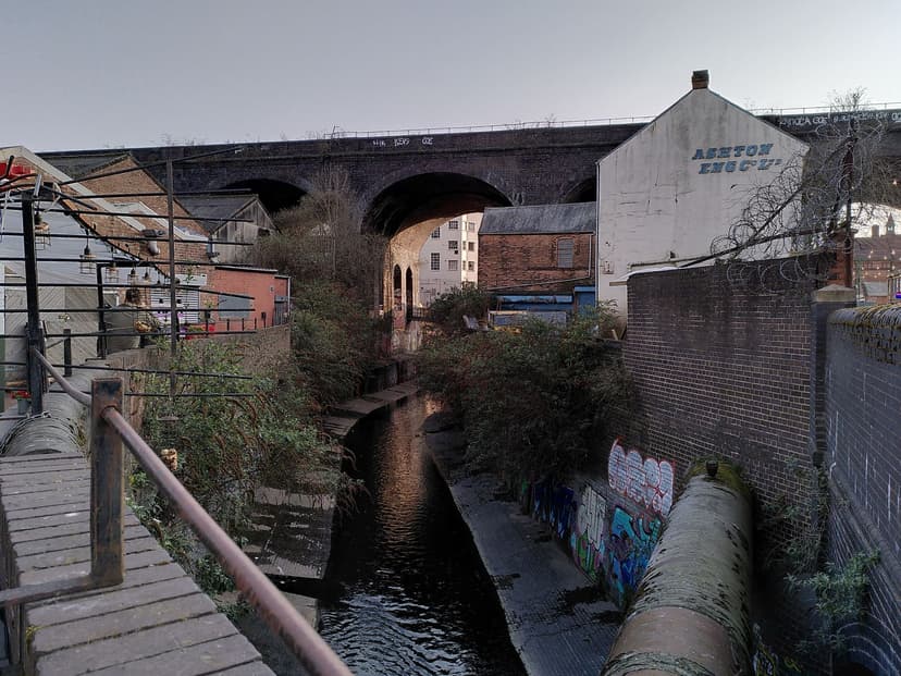 A shallow river in a deep brick-walled channel between buildings.