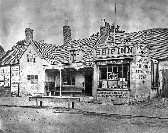 Old photograph of a low inn with a verandah and a signboard reading “The Old Ship Inn Established 1560”.