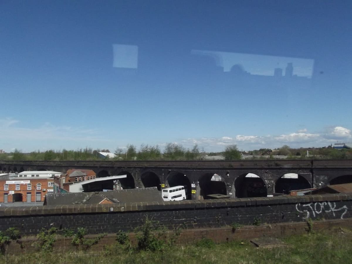 A long row of dark brick arches with workshops beneath and scrub on top.