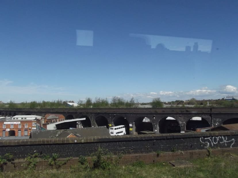 A long row of dark brick arches with workshops beneath and scrub on top.