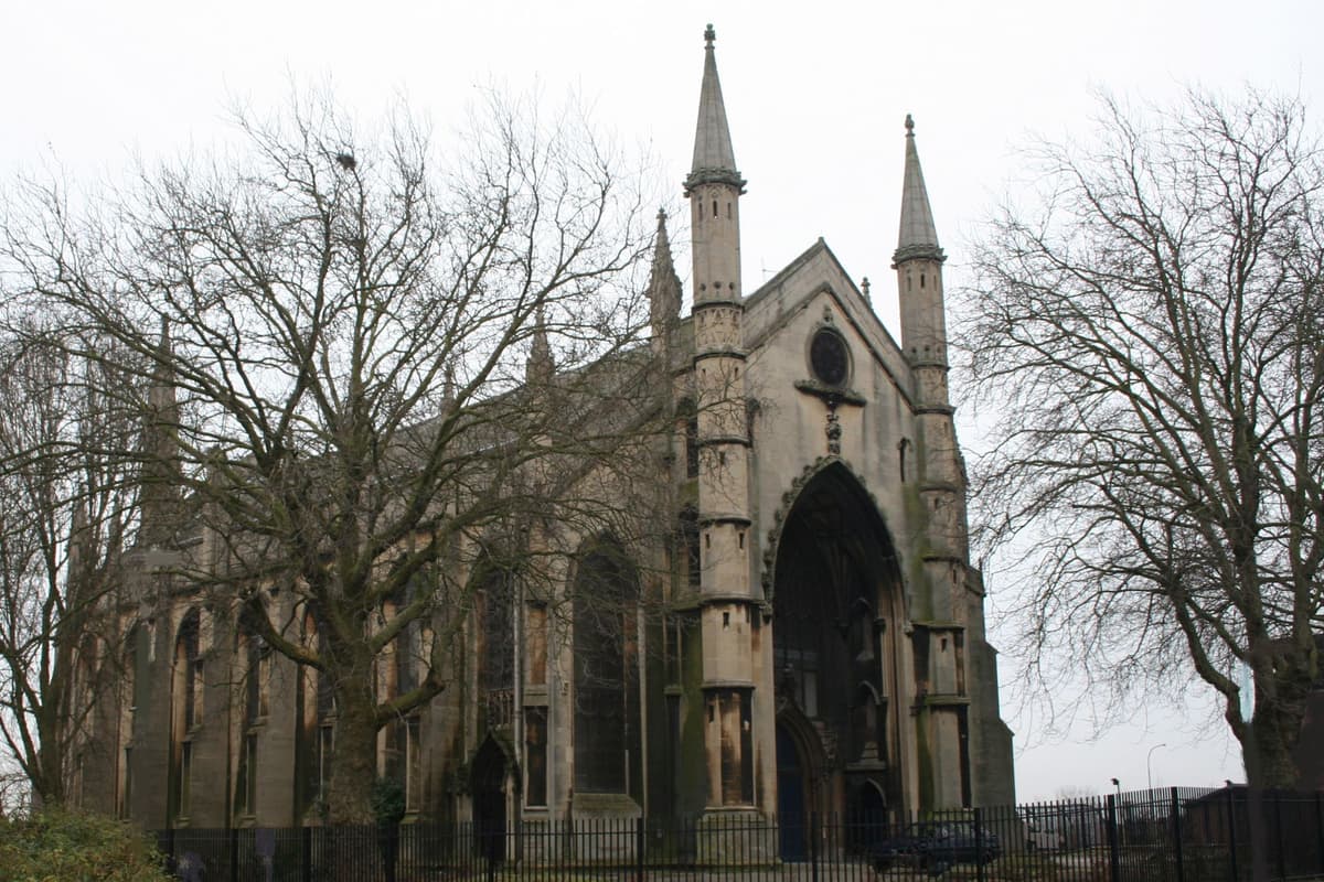 Pale stone Gothic church front with a tall recessed arch flanked by octagonal pinnacled turrets.
