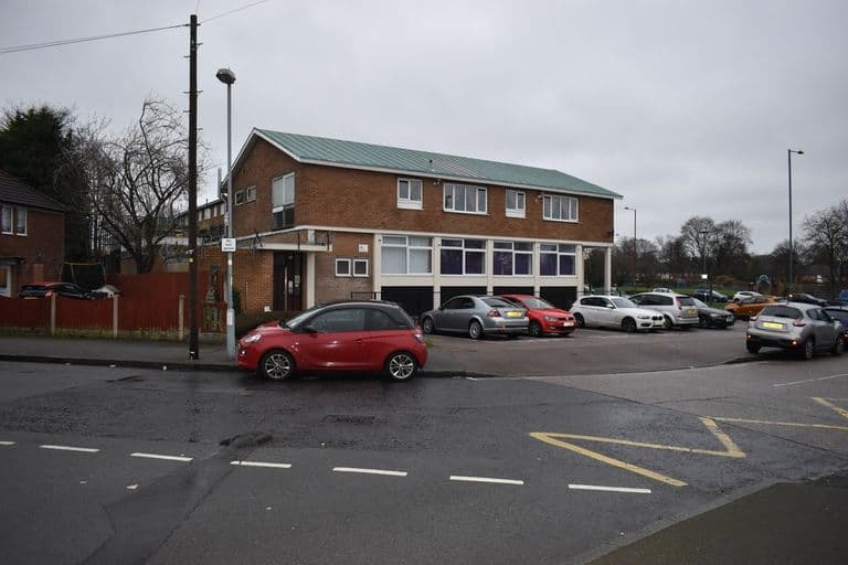 Two-storey brick library building with a band of windows on the ground floor, facing a car park near the Circle